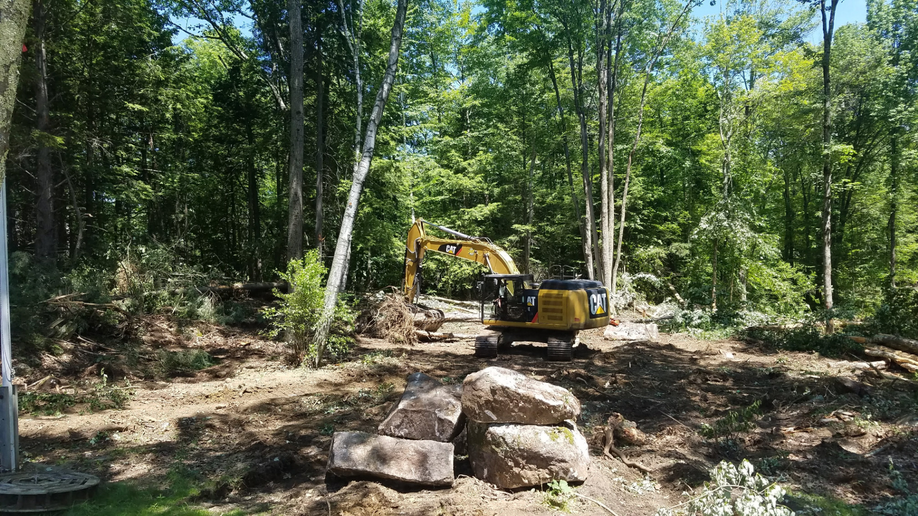 Excavator working around large boulders on a wooded Hilltown property