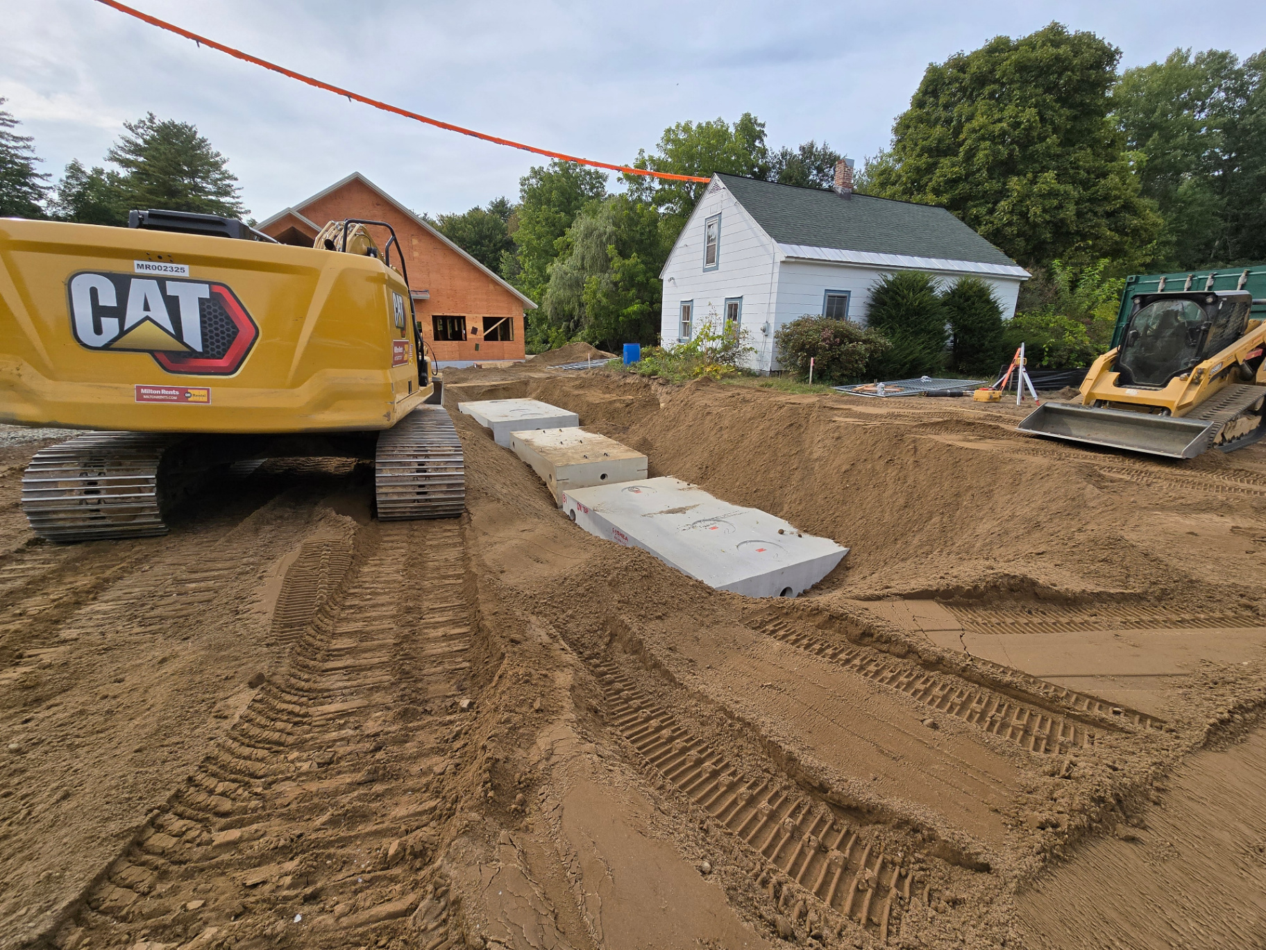 Septic tanks, risers, excavation equipment, and sitework during a residential system installation.
